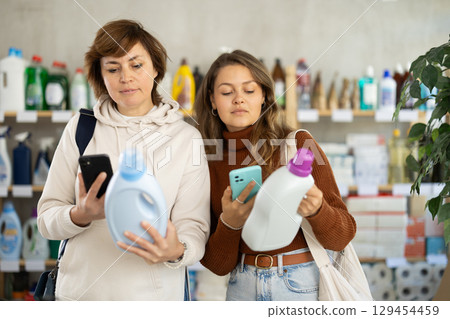 Two women checking expiration date of detergent using her smartphone in supermarket 129454459