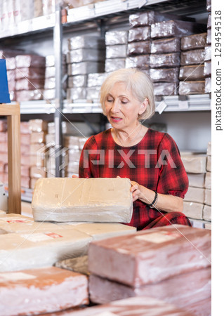Elderly woman chooses pottery clay in shop 129454518