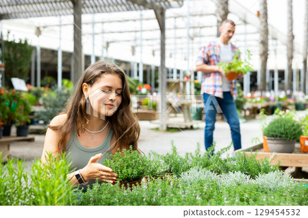In flower shop, girl customer chooses thymus plant to decorate room, balcony, terrace 129454532