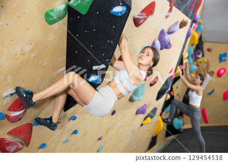 Young woman practicing rock climbing on climbing wall 129454538