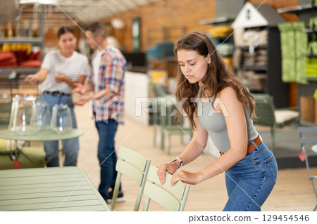 Pensive girl choosing patio chairs at garden furniture store Pensive girl choosing patio chairs at garden furniture store 129454546