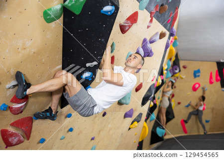 Young man practicing rock climbing on climbing wall 129454565