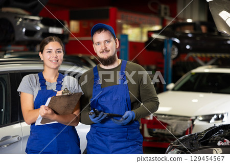 Portrait of two auto mechanics - man and girl against the background of cars in car service center 129454567
