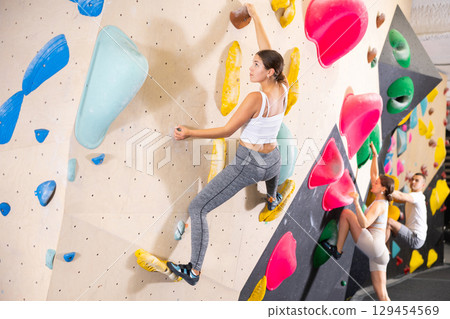 Young woman climbs steep artificial wall in sports complex and trains endurance 129454569