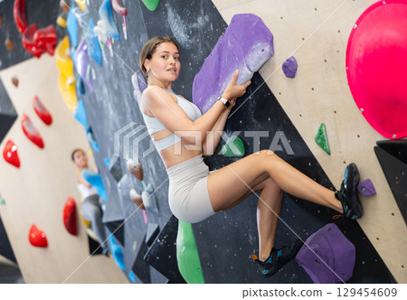 Young woman climbs steep artificial wall in sports complex and trains endurance Young woman climbs steep artificial wall in sports complex and trains endurance 129454609