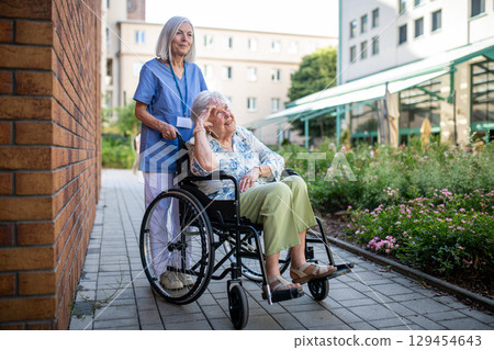 Aging woman in wheelchair enjoying fresh air with care assistant Aging woman in wheelchair enjoying fresh air with care assistant 129454643