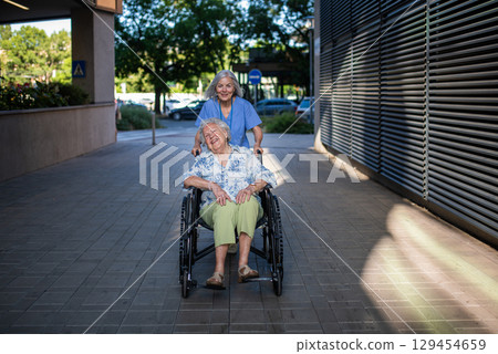 Older caregiver pushing senior woman in wheelchair. 129454659