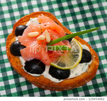 Toast with salmon, olives and creamy sauce on checkered textile 129454662