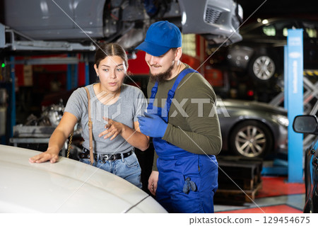 Girl explains and shows the auto mechanic the damaged areas on her car in auto repair shop 129454675