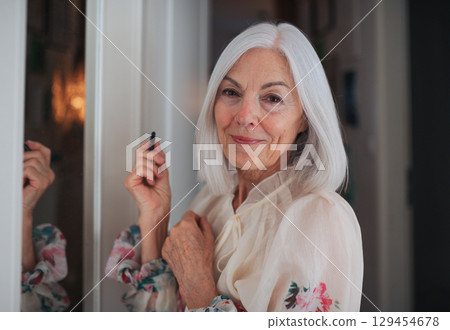 Senior woman applying makeup in front of mirror. Senior woman applying makeup in front of mirror. 129454678