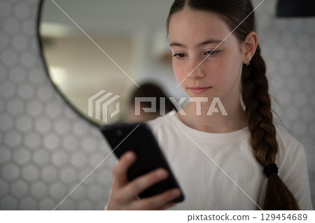 Young girl standing in bathroom and checking her smartphone. Young girl standing in bathroom and checking her smartphone. 129454689