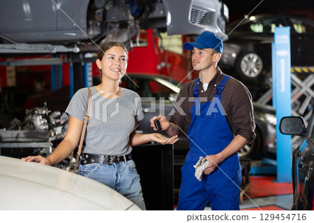 Kind car mechanic handing over the keys of car to glad female client in auto shop Kind car mechanic handing over the keys of car to glad female client in auto shop 129454716
