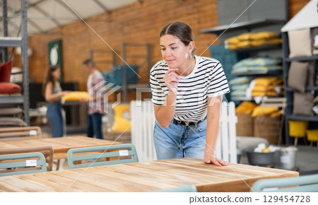 Interested girl choosing comfortable garden table in store Interested girl choosing comfortable garden table in store 129454728