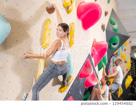 Young woman climbs steep artificial wall in sports complex and trains endurance Young woman climbs steep artificial wall in sports complex and trains endurance 129454882