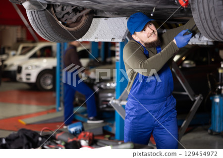 Skilled male auto mechanic in blue overalls repairing automobile 129454972