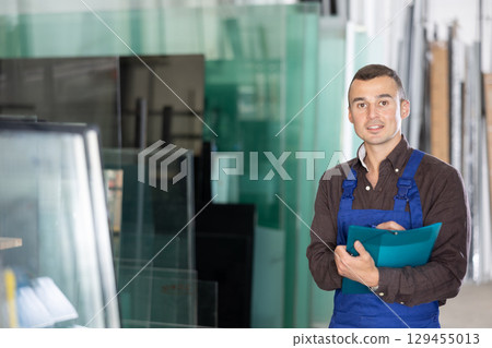 Experienced worker checks the quality of made window glass in an industrial workshop, marks the data in documents 129455013
