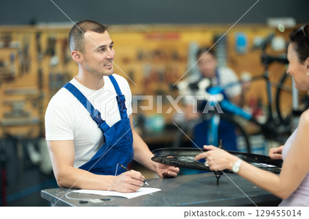 Bicycle technician writing repair checklist and discussing with female client Bicycle technician writing repair checklist and discussing with female client 129455014