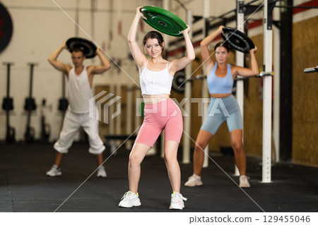 Closeup of athletic sports girl standing with plate of barbell in hands in fitness studio 129455046