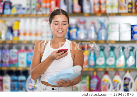 Girl examines liquid laundry detergent in supermarket department and scans QR code on package 129455076