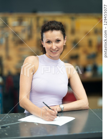 Smiling woman filling forms in bike repair shop 129455077