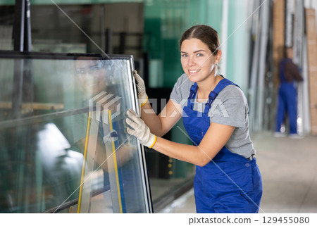 Female glazier controlling quality of sheet glass in workroom 129455080