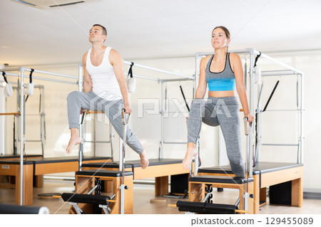 Young man and woman performing Pilates exercises on Wunda chairs 129455089
