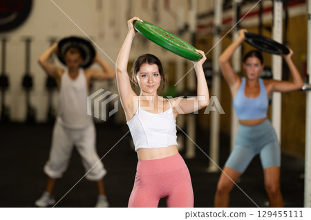 Closeup of athletic sports girl standing with plate of barbell in hands in fitness studio 129455111