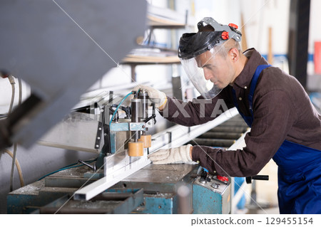 Glass workshop - man works on machine for cutting aluminum profiles for windows Glass workshop - man works on machine for cutting aluminum profiles for windows 129455154