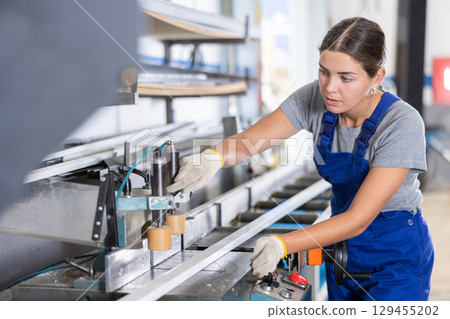 Glass workshop - girl works on machine for cutting aluminum profiles for windows Glass workshop - girl works on machine for cutting aluminum profiles for windows 129455202