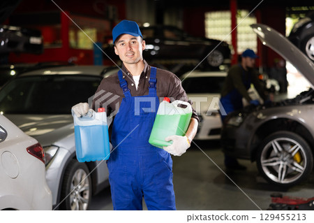 Positive male worker of car workshop holding full plastic cans 129455213