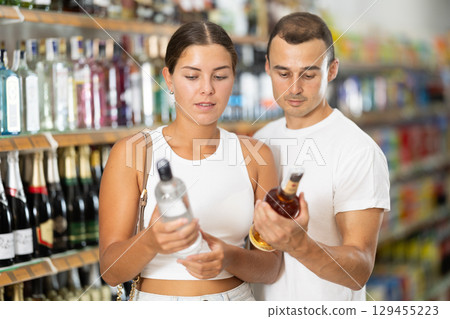 Married couple chooses alcoholic drinks in supermarket - vodka, champagne or whiskey 129455223