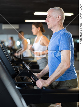 Elderly man exercising on treadmill in gym 129455224