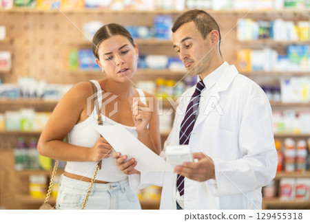 Male pharmacist consulting young girl about medicament in box 129455318