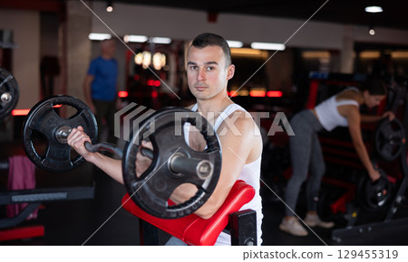 Sporty man performing set of exercises with barbell during intense workout Sporty man performing set of exercises with barbell during intense workout 129455319