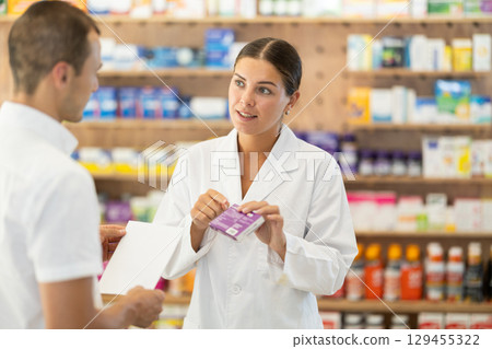 Female pharmacist consulting young guy about medicament according to recipe Female pharmacist consulting young guy about medicament according to recipe 129455322