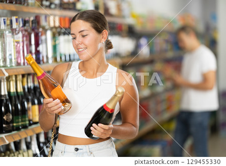 Woman chooses bottle of champagne in shop store Woman chooses bottle of champagne in shop store 129455330