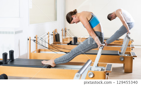 Young girl performing pilates exercises on reformer at group workout 129455340