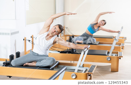 Man doing stretching exercises on Pilates reformer in fitness center 129455343