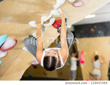 Young woman climbs steep artificial wall in sports complex and trains endurance Young woman climbs steep artificial wall in sports complex and trains endurance 129455364