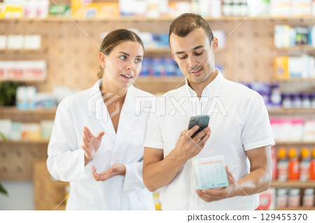 In pharmacy man customer scans QR code on label box, photographs packaging in presence of employee In pharmacy man customer scans QR code on label box, photographs packaging in presence of employee 129455370