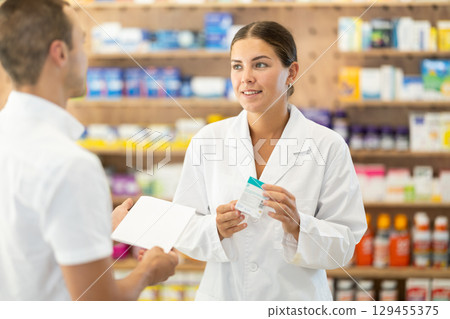Female pharmacist consulting young guy about medicament according to recipe Female pharmacist consulting young guy about medicament according to recipe 129455375