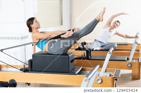 Sporty girl doing V-sit on Pilates reformer with box and straps Sporty girl doing V-sit on Pilates reformer with box and straps 129455414