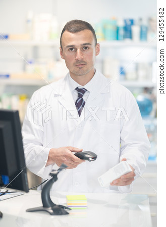 Young male pharmacist pushing medicine at cash register Young male pharmacist pushing medicine at cash register 129455482
