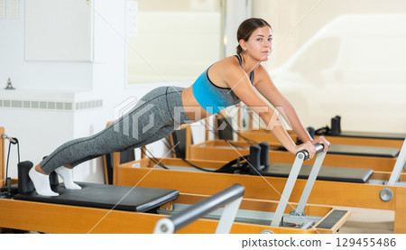 Young girl performing pilates exercises on reformer in studio 129455486