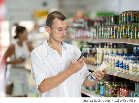Male shopper scanning barcode or qr code with smartphone on mayonnaise label 129455499