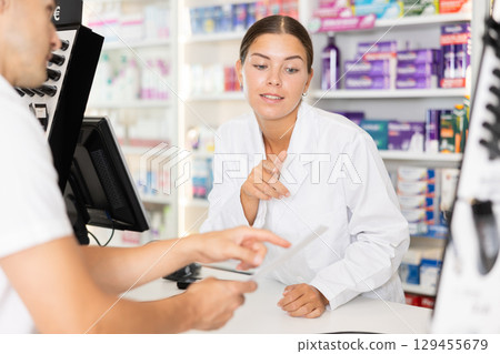 Girl pharmacist near cash register area serves customer, answers questions 129455679