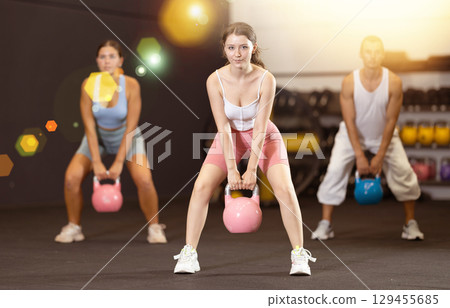 Young woman lifting kettlebell in gym 129455685