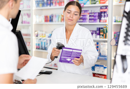 Girl pharmacist near cash register area serves customer, scans product and selling drugs Girl pharmacist near cash register area serves customer, scans product and selling drugs 129455689