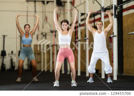 Young girl working out with other athletes with resistance band, strong biceps or abdominal muscles in gym Young girl working out with other athletes with resistance band, strong biceps or abdominal muscles in gym 129455700