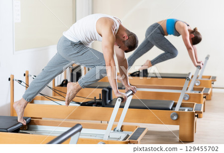 Sporty man in sports wear engages in Pilates on reformer machine Sporty man in sports wear engages in Pilates on reformer machine 129455702